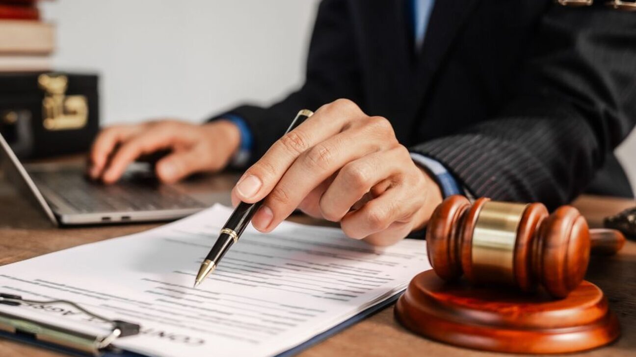 Hands on computer and paper near a judge's gavel.