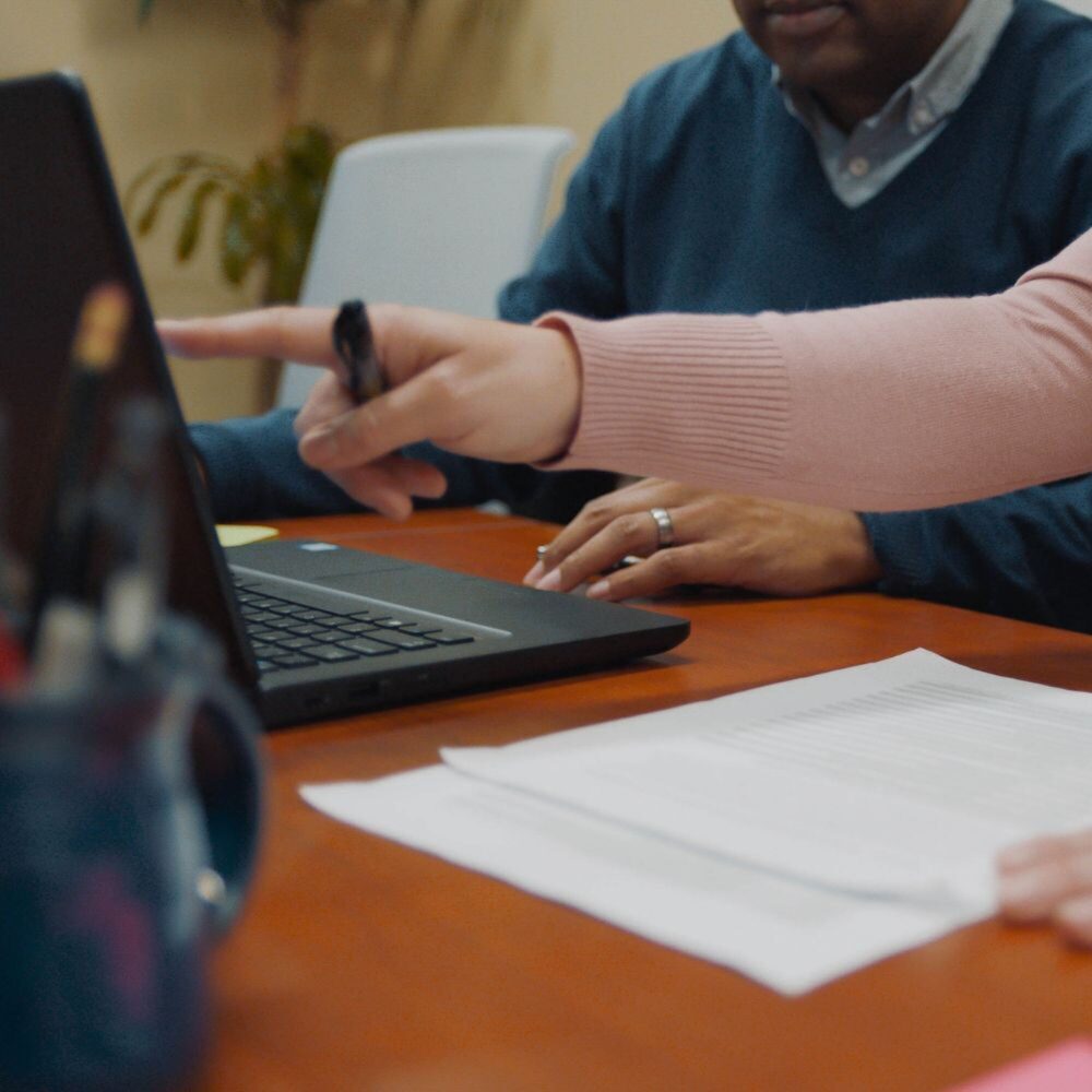 Two people's hands working and pointing to a computer screen.