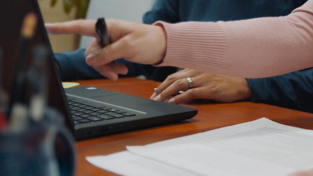 Two people's hands working and pointing to a computer screen.