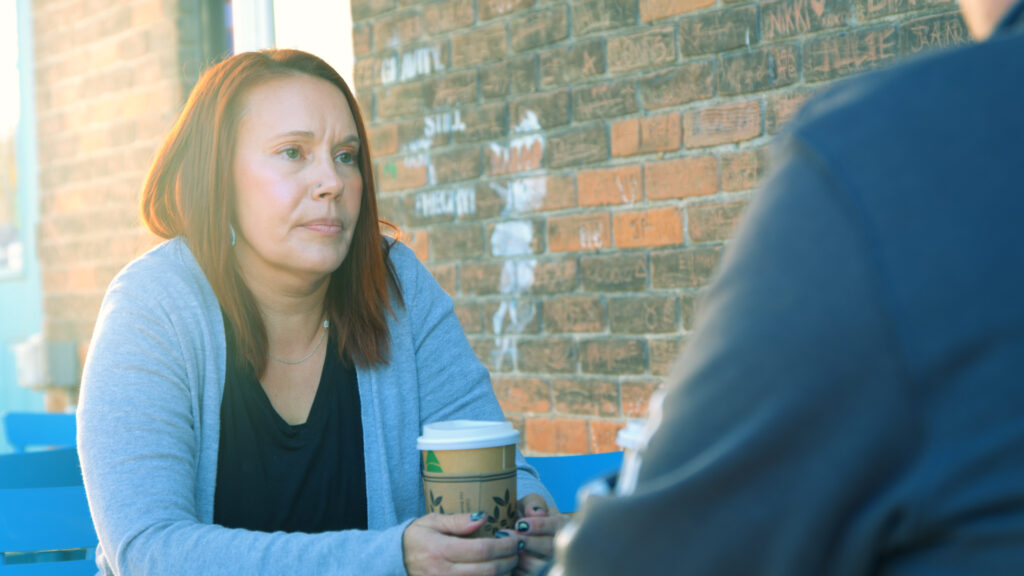 Woman with coffee listening to sits outside listening to someone sitting across fomr her.