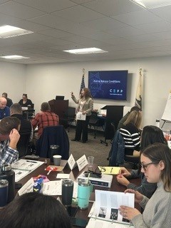 People sit and review information as a woman stands and speaks about pretrial fundamentals during a training.